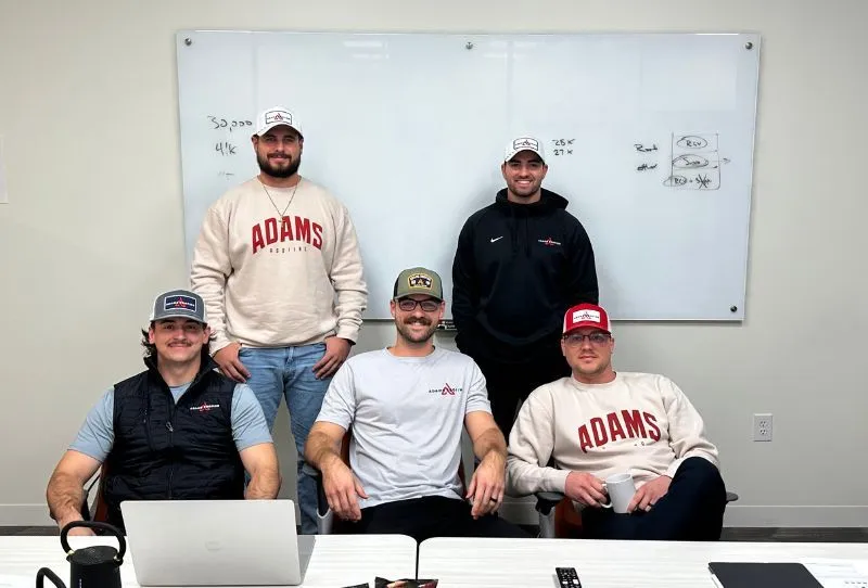Five men wearing 'ADAMS' branded apparel pose in an office setting