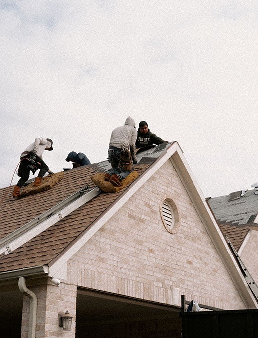 Two workers install dark shingles over synthetic underlayment on a residential roof